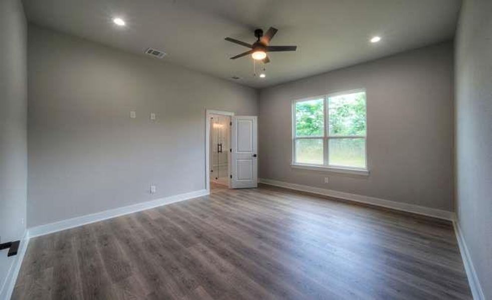 Laminate wood flooring and a refreshing ceiling fan create comfort in this airy bedroom.