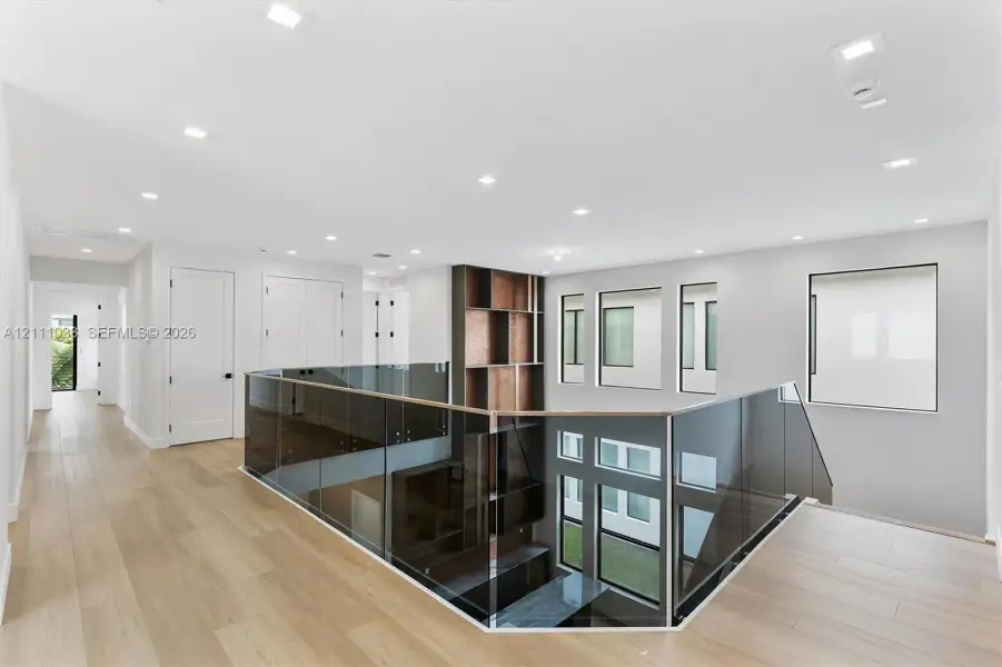 Open landing featuring wood-finish flooring, recessed lighting, glass paneled railings, and floor-to-ceiling built-in shelving