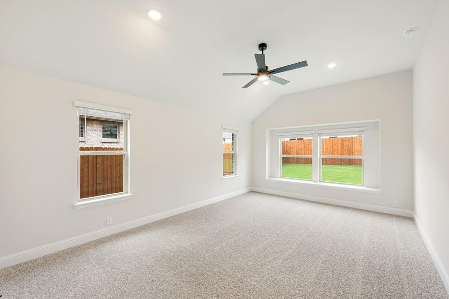 Empty bedroom with vaulted ceiling, ceiling fan, carpet flooring, and large windows overlooking backyard Empty bedroom with vaulted ceiling, ceiling fan, carpet flooring, and large windows overlooking backyard