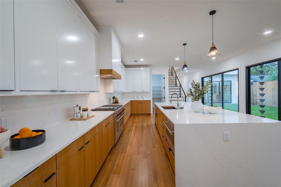 Kitchen with light stone countertops, white cabinets, sink, pendant lighting, and double oven range