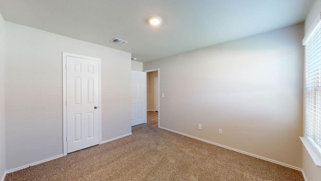A well-proportioned bedroom offers carpet flooring and a window providing natural light.