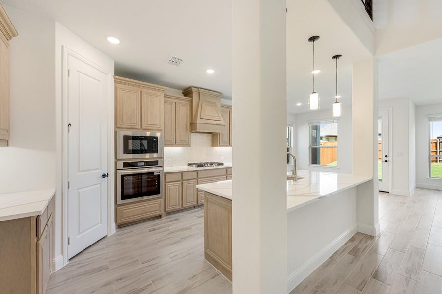 Kitchen with light wood cabinets, stainless steel appliances, white island, and pendant lights over breakfast bar. Kitchen with light wood cabinets, stainless steel appliances, white island, and pendant lights over breakfast bar.