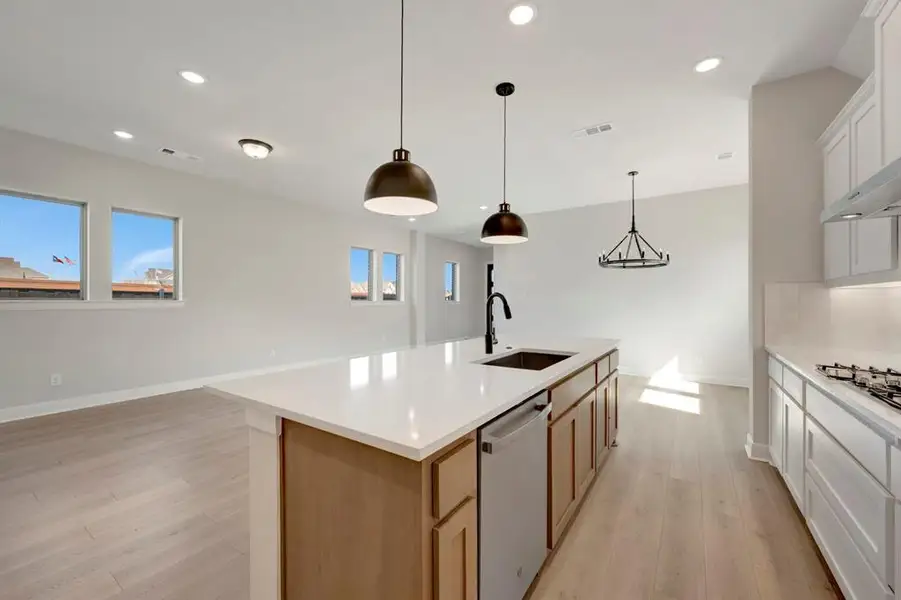 Two tone kitchen with two tone cabinets, hanging light fixtures, light wood-style flooring, stainless steel appliances, and a kitchen island with sink