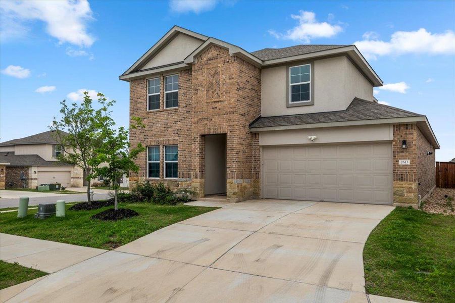Brick and stucco facade home featuring a two-car garage, concrete driveway, and front landscaping