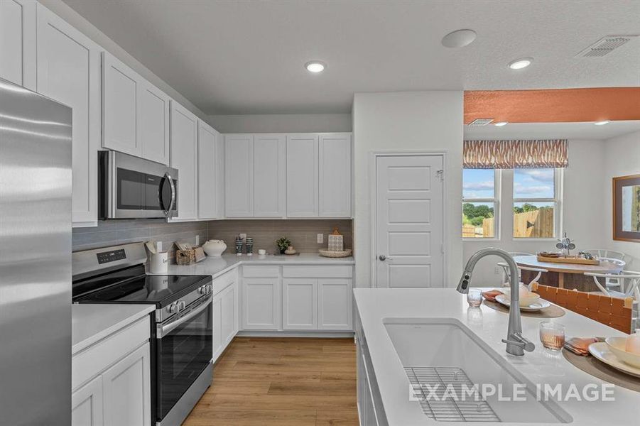 Kitchen featuring decorative backsplash, appliances with stainless steel finishes, white cabinetry, and sink