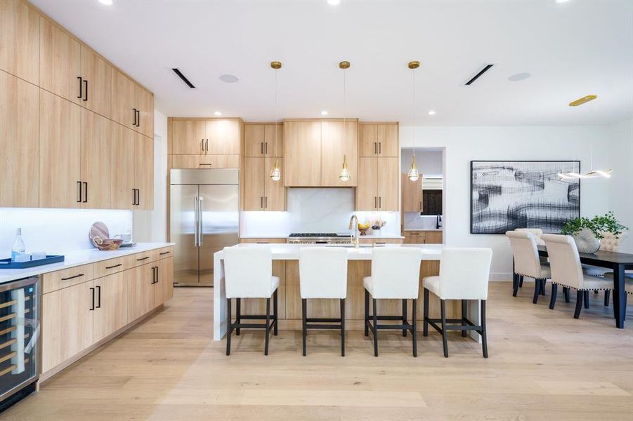 Kitchen with decorative light fixtures, beverage cooler, built in fridge, and light brown cabinets