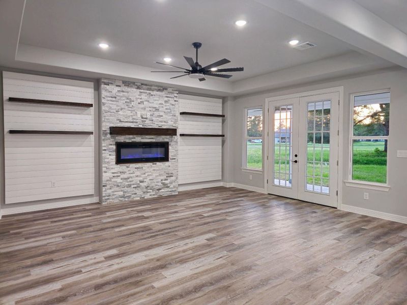 Living room with a stone fireplace, built-in floating shelving, over shiplap accent wall.