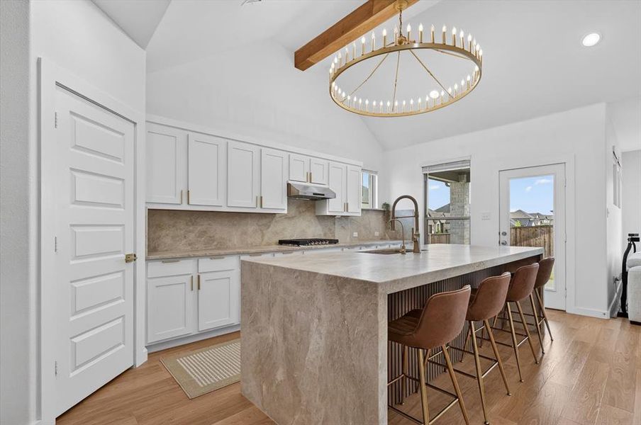 Modern kitchen featuring light wood-finish flooring, white cabinetry, and a large central island with a waterfall countertop