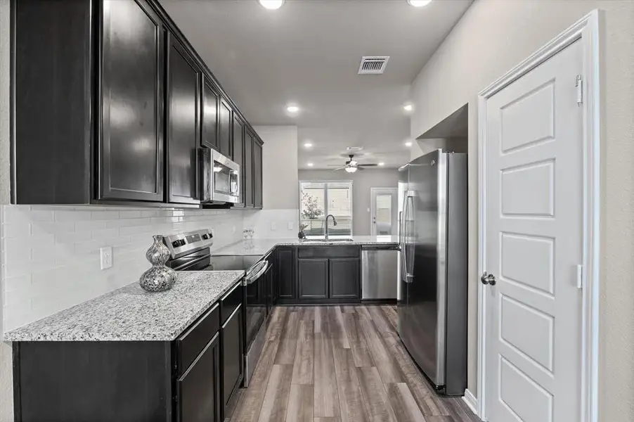 Kitchen with appliances with stainless steel finishes, light stone countertops, dark wood-style flooring, tasteful backsplash, and recessed lighting Kitchen with appliances with stainless steel finishes, light stone countertops, dark wood-style flooring, tasteful backsplash, and recessed lighting