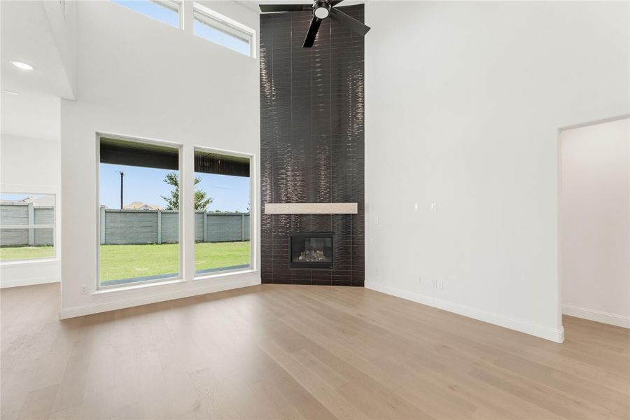 Open living room with high ceilings, dark tile fireplace surround, hardwood floors, and large windows overlooking backyard