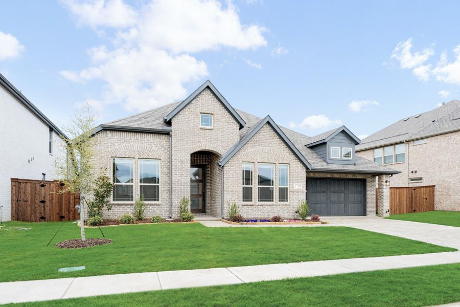 Single-story brick home with arched entry, two-car garage, and manicured front lawn