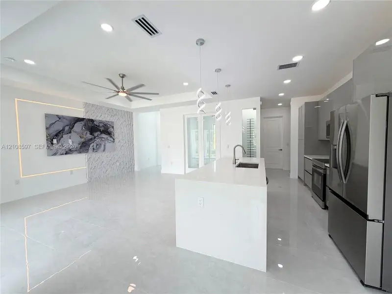 Open-concept kitchen featuring an expansive quartz-topped island, high-gloss cabinetry, stainless steel appliances, recessed lighting, and a stone-accented wall with integrated perimeter lighting