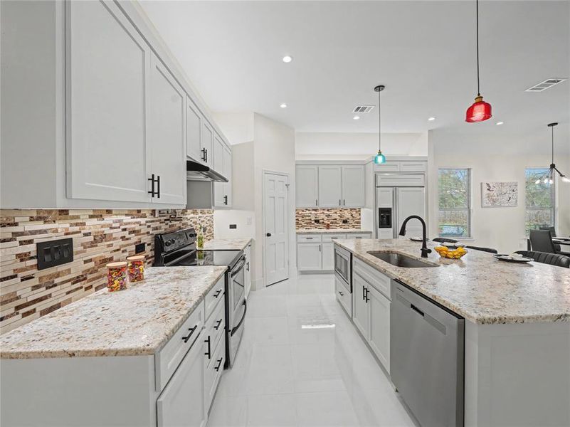 Kitchen with built in appliances, light stone countertops, a center island with sink, hanging light fixtures, and light tile patterned floors