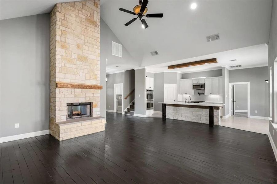 Unfurnished living room with high vaulted ceiling, a stone fireplace, ceiling fan, dark wood-type flooring, and stairway