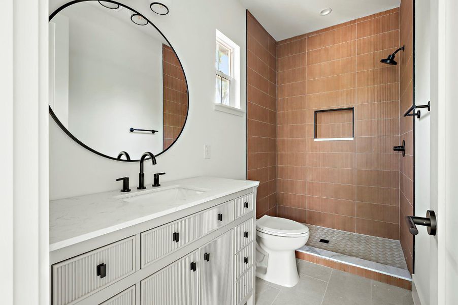 Full bathroom with tiled shower, tile patterned floors, toilet, and vanity
