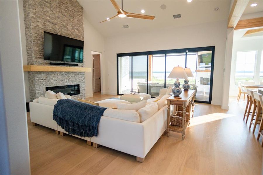 Living room featuring a stone fireplace, light wood-style floors, recessed lighting, high vaulted ceiling, and ceiling fan Living room featuring a stone fireplace, light wood-style floors, recessed lighting, high vaulted ceiling, and ceiling fan