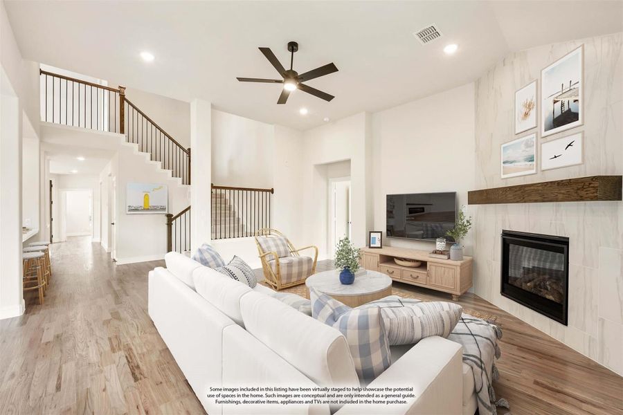 Open living room with high ceilings, fireplace, ceiling fan, and staircase with hardwood floors