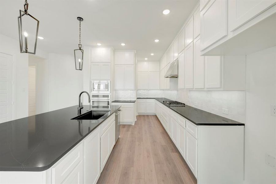 Kitchen featuring light wood-style floors, a center island with sink, and white cabinets Kitchen featuring light wood-style floors, a center island with sink, and white cabinets