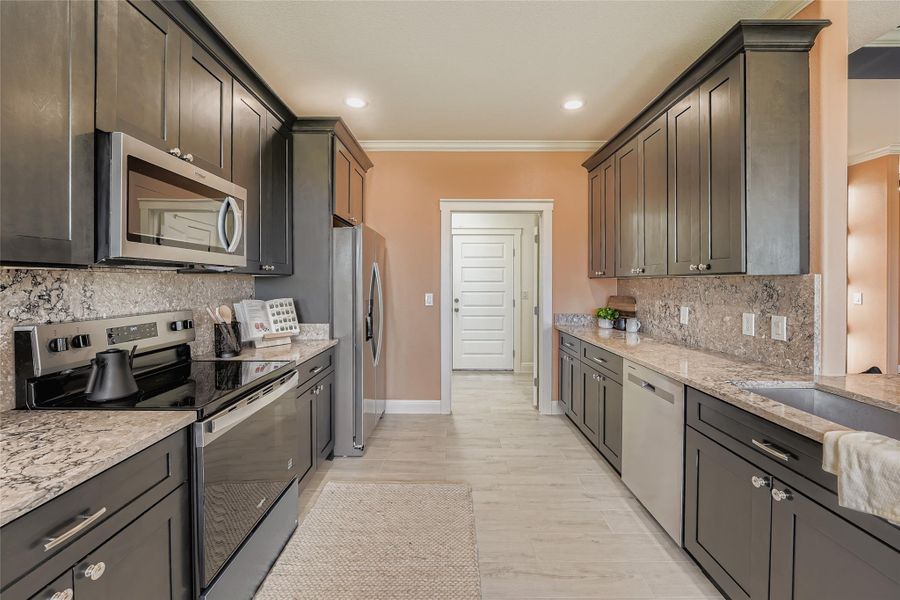 Kitchen featuring stainless steel appliances, tasteful backsplash, light stone counters, crown molding, and light wood-style floors