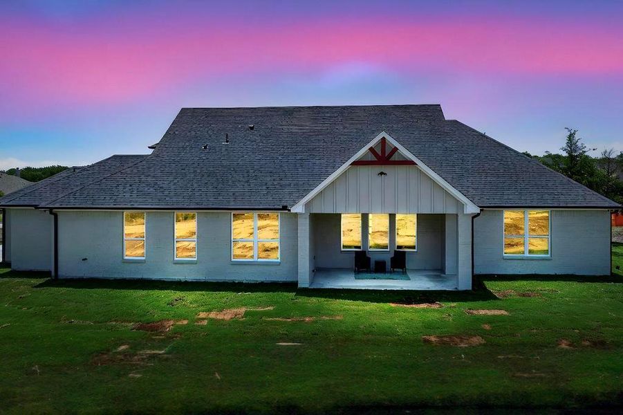 Back of property at dusk with a yard and roof with shingles