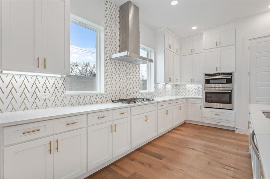 Kitchen with stainless steel appliances, a healthy amount of sunlight, light hardwood / wood-style floors, and wall chimney exhaust hood