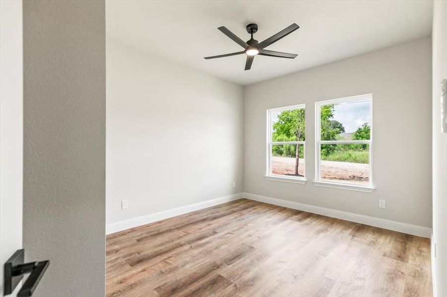 Interior room featuring wood-finish flooring, two large windows, a ceiling fan with integrated lighting, and neutral wall paint