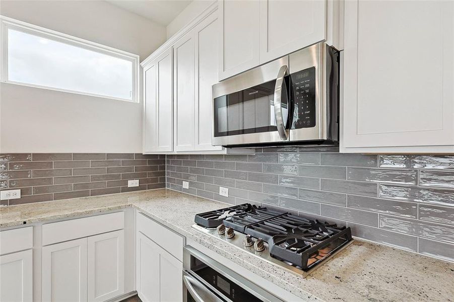 Kitchen featuring appliances with stainless steel finishes, decorative backsplash, white cabinets, and light stone countertops