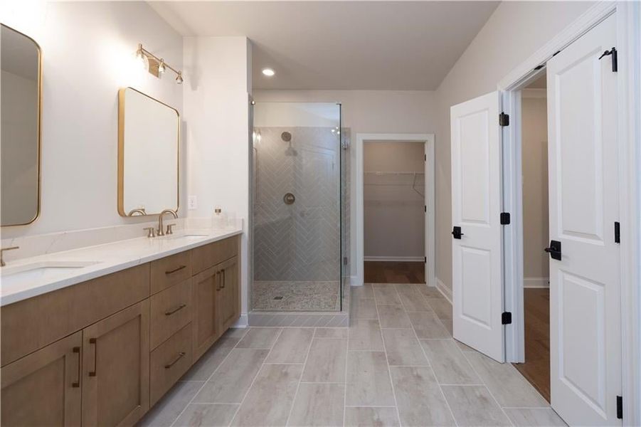 Full bathroom with double vanity, a walk in closet, a stall shower, and recessed lighting
