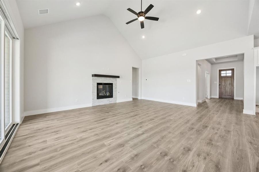 Unfurnished living room with light wood-style floors, high vaulted ceiling, a glass covered fireplace, a ceiling fan, and recessed lighting