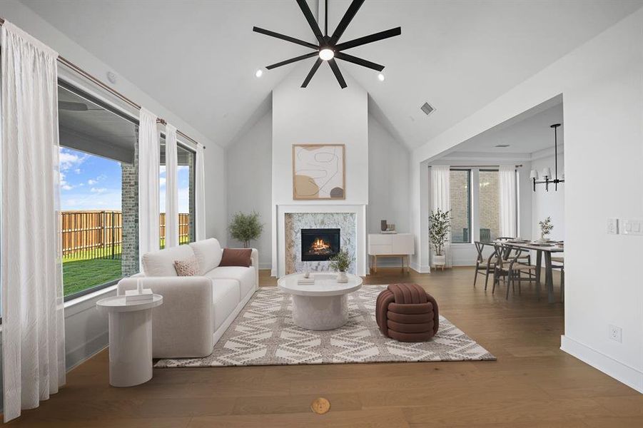 Living area with a warm lit fireplace, wood finished floors, high vaulted ceiling, recessed lighting, and a chandelier