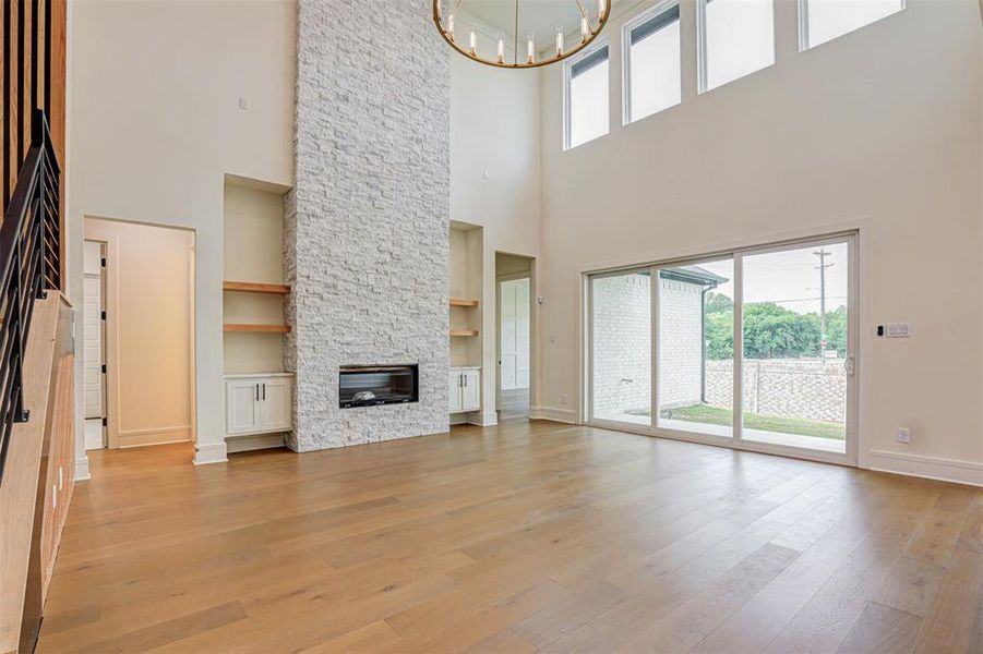 Unfurnished living room featuring a high ceiling, a chandelier, light wood finished floors, a fireplace, and built in shelves