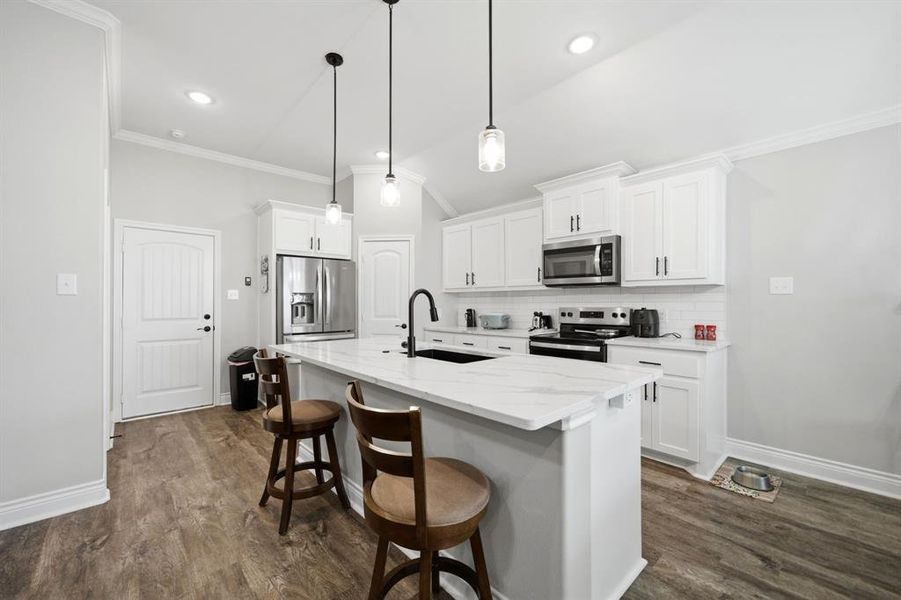 Kitchen with a breakfast bar area, stainless steel appliances, white cabinetry, dark wood-style floors, and a center island with sink