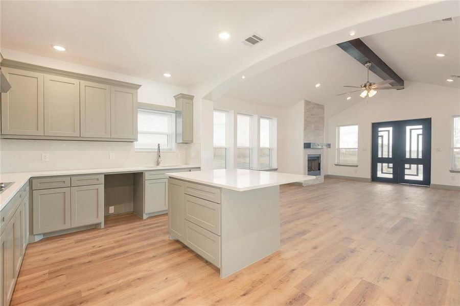 Kitchen featuring light wood-type flooring, open floor plan, a kitchen island, recessed lighting, and a large fireplace