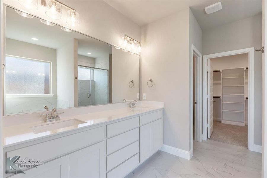 Full bath with a marble finish shower, double vanity, a walk in closet, and light marble finish flooring