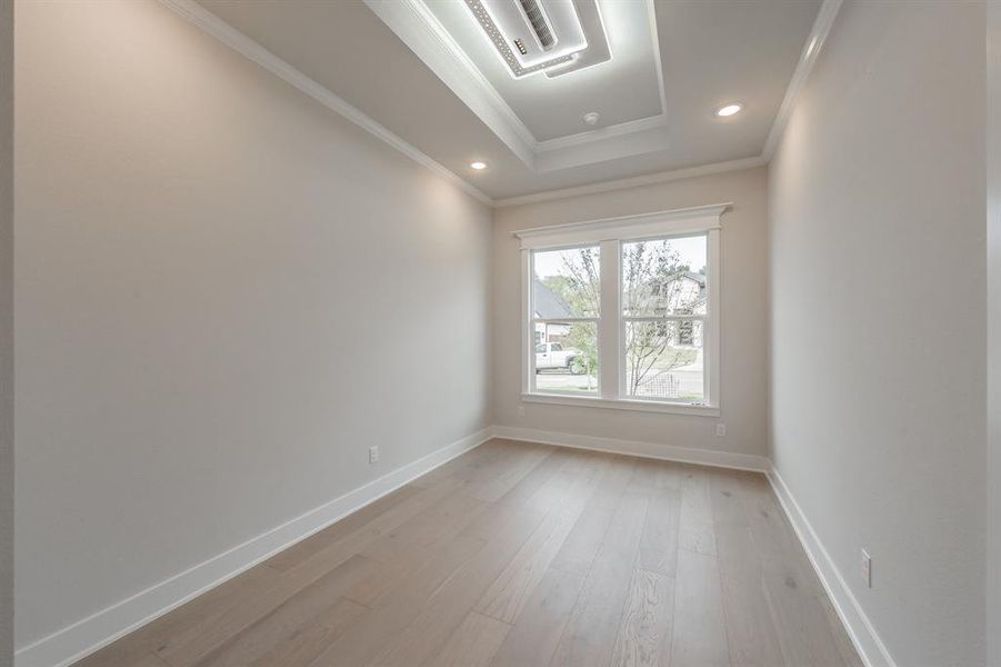 Spare room featuring cooling unit, light wood finished floors, a raised ceiling, ornamental molding, and recessed lighting