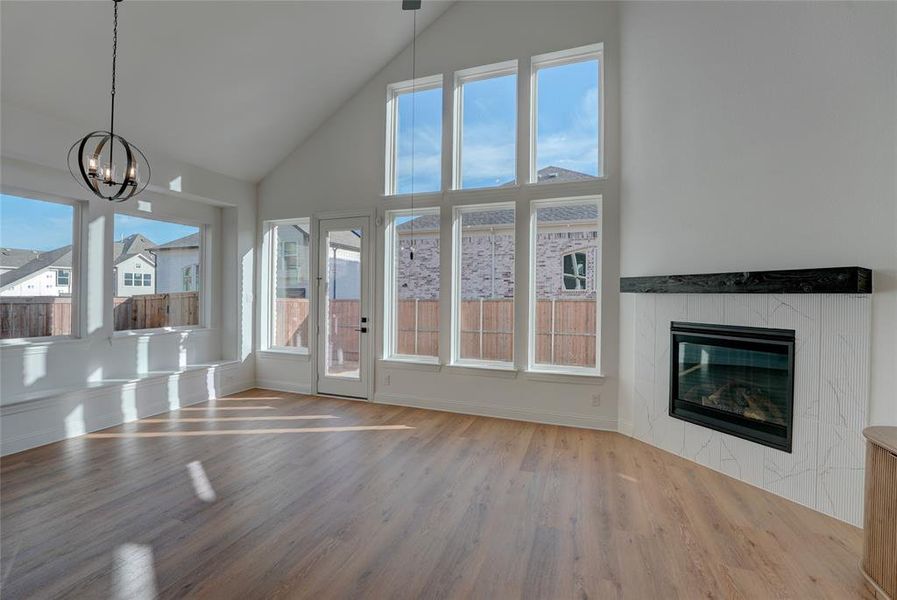 Living room featuring baseboards, a tiled fireplace, vinyl floors, an inviting chandelier, and high vaulted ceiling