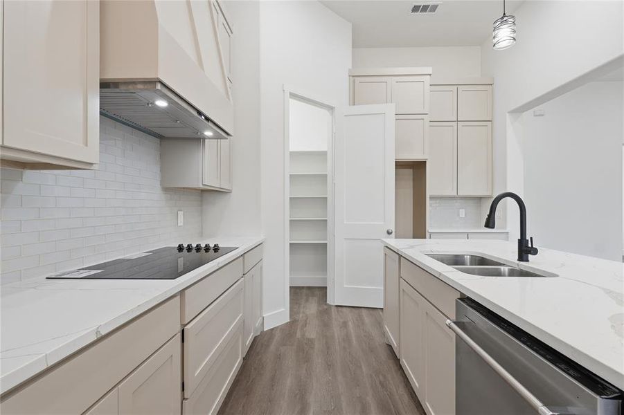Modern kitchen featuring light-toned cabinetry, white countertops, a black cooktop, stainless steel appliances, and wood-finish flooring