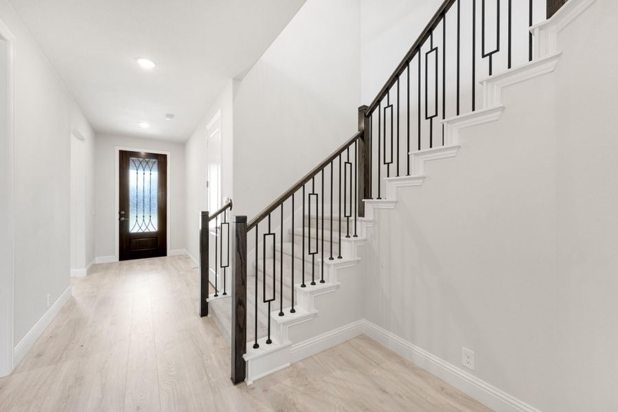 Entryway with staircase featuring dark wood handrail, black iron balusters, and light hardwood floors leading to a glass-panel front door