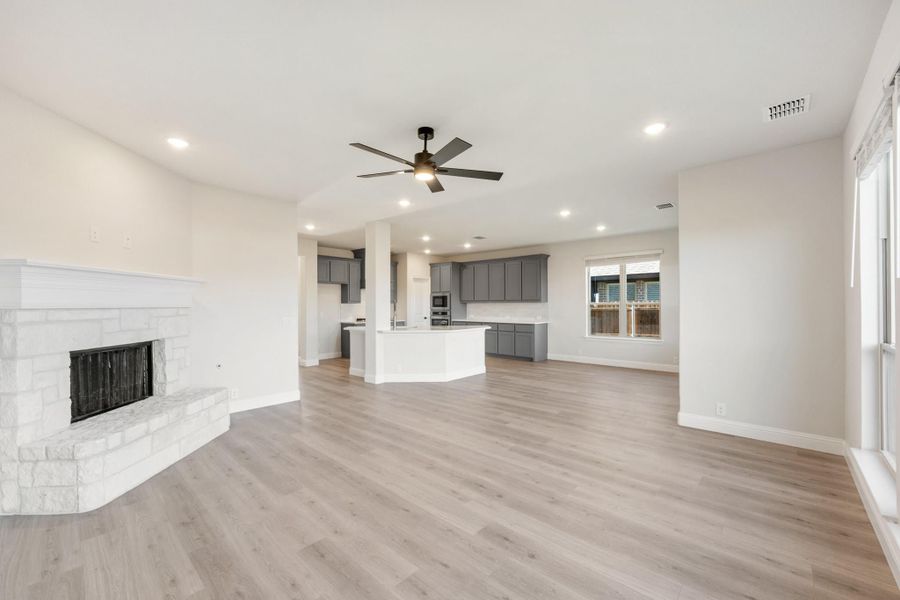 Open living area with stone fireplace, hardwood floors, and open-concept kitchen with gray cabinets in background Open living area with stone fireplace, hardwood floors, and open-concept kitchen with gray cabinets in background