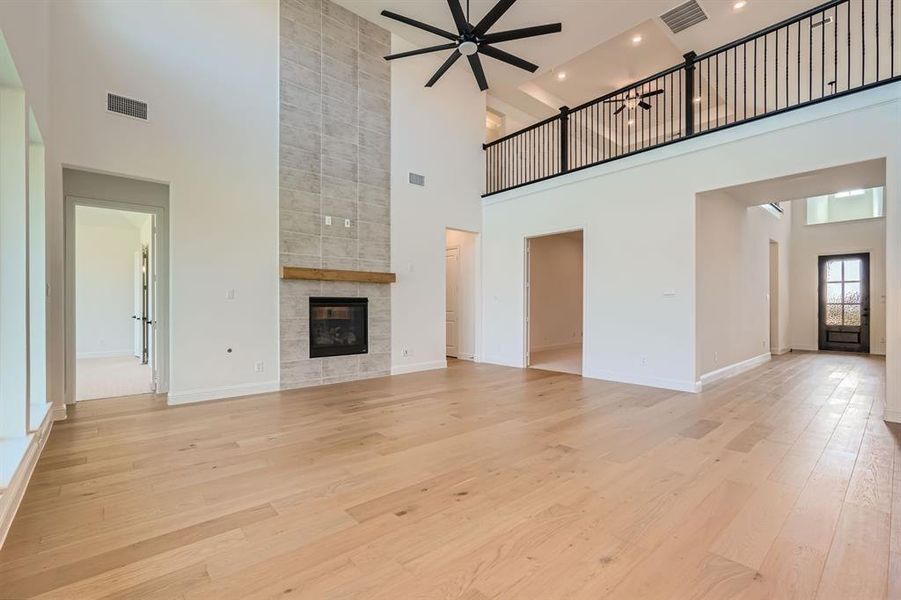 Unfurnished living room with a fireplace, a towering ceiling, light hardwood / wood-style floors, and ceiling fan