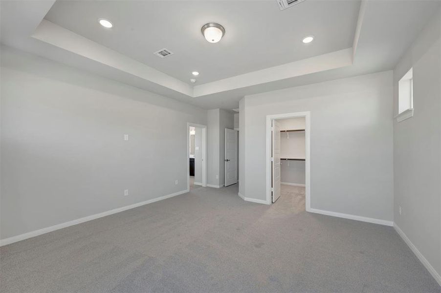 Unfurnished bedroom with carpet floors, a spacious closet, recessed lighting, and a raised ceiling