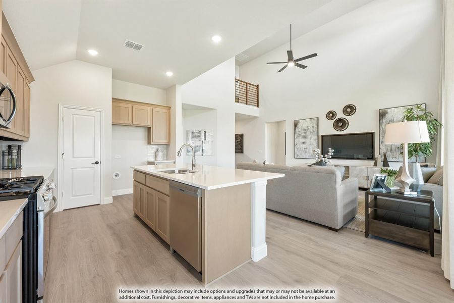 Open-concept kitchen with island sink flowing into living room, high ceilings, light wood cabinets, and hardwood floors