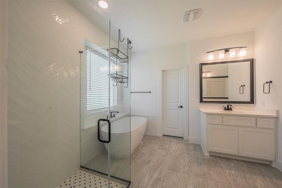 Primary Bathroom featuring a glass-enclosed shower with white herringbone tile, a freestanding bathtub, and a vanity with a white countertop and framed mirror