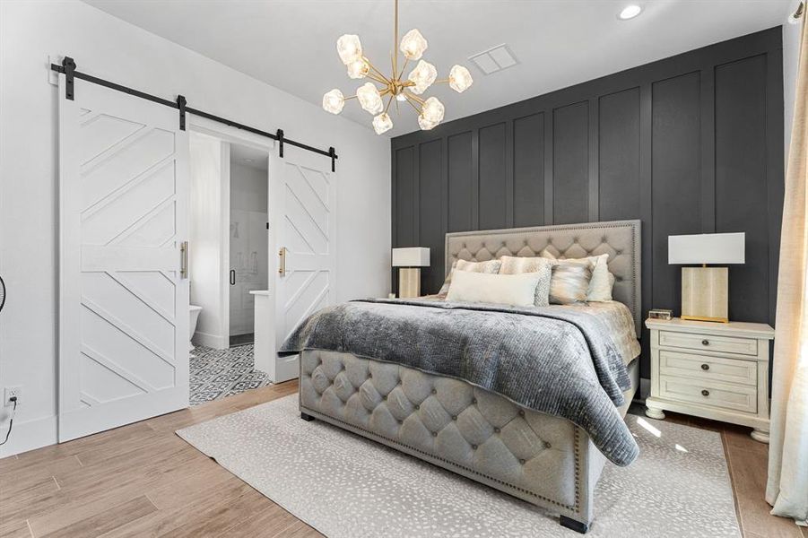 Bedroom with a barn door, a decorative wall, wood finished floors, a chandelier, and visible vents Bedroom with a barn door, a decorative wall, wood finished floors, a chandelier, and visible vents