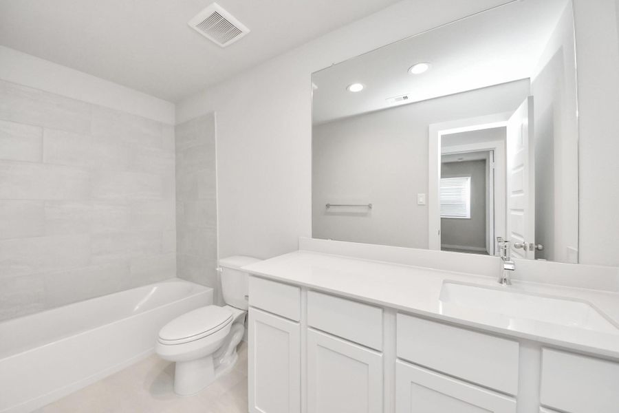 Secondary bath features tile flooring, bath/shower combo with tile surround, light stained wood cabinets, beautiful light countertop.