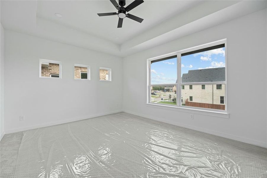 Unfurnished room with a ceiling fan, a raised ceiling, and carpet Unfurnished room with a ceiling fan, a raised ceiling, and carpet