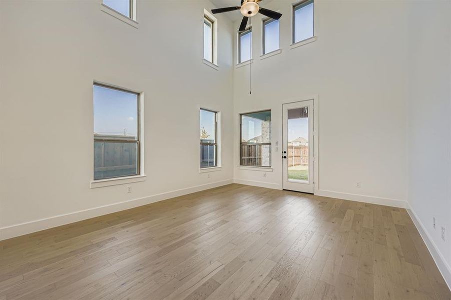 Spare room with light wood-style floors, a ceiling fan, and a towering ceiling