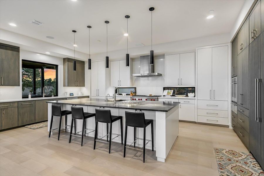 Dual tone kitchen with an island with sink, hanging light fixtures, a kitchen bar, modern cabinets, and dark stone counters Dual tone kitchen with an island with sink, hanging light fixtures, a kitchen bar, modern cabinets, and dark stone counters