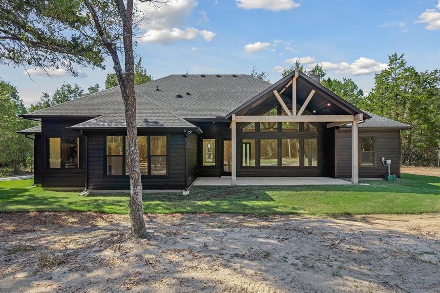 Back of house featuring a patio area, roof with shingles, and a yard