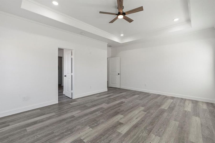 Unfurnished room featuring ceiling fan, wood-type flooring, ornamental molding, and a tray ceiling